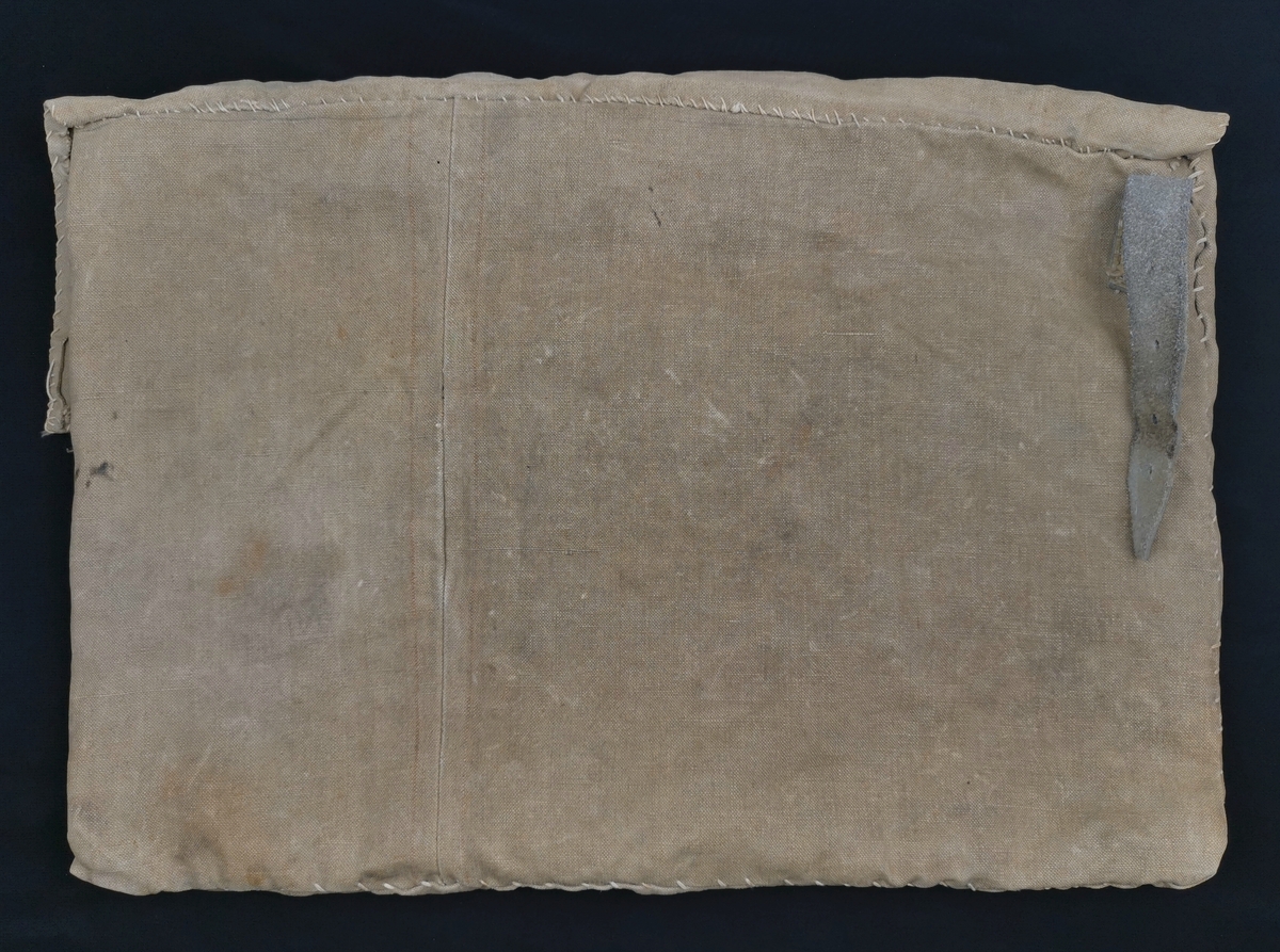 Tøyveske laget av Magdalon B. Andersen under hans fangenskap i Sachsenhausen (1943-45). Veska har en klaff som kan lukkes med tre knapper. På venstreside er påsydd ei lærrem (21 cm). På forsida er fangenummeret fra Sachsenhausen påskrevet. Veska fulgte Magdalon Andersen hele livet, som oppbevaringssted for papirer fra fangenskapet.