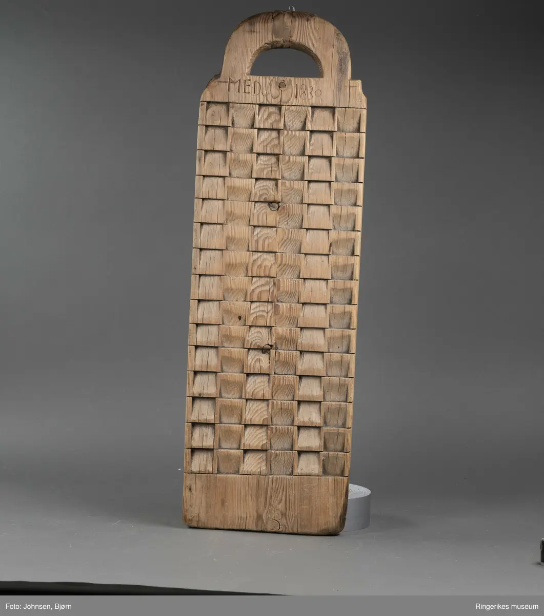 Vaskebrett i furu med kvadrater skråskjært i vekselsvis motsatt retning, sånn at rillene går i begge retninger. Håndtak øverst.