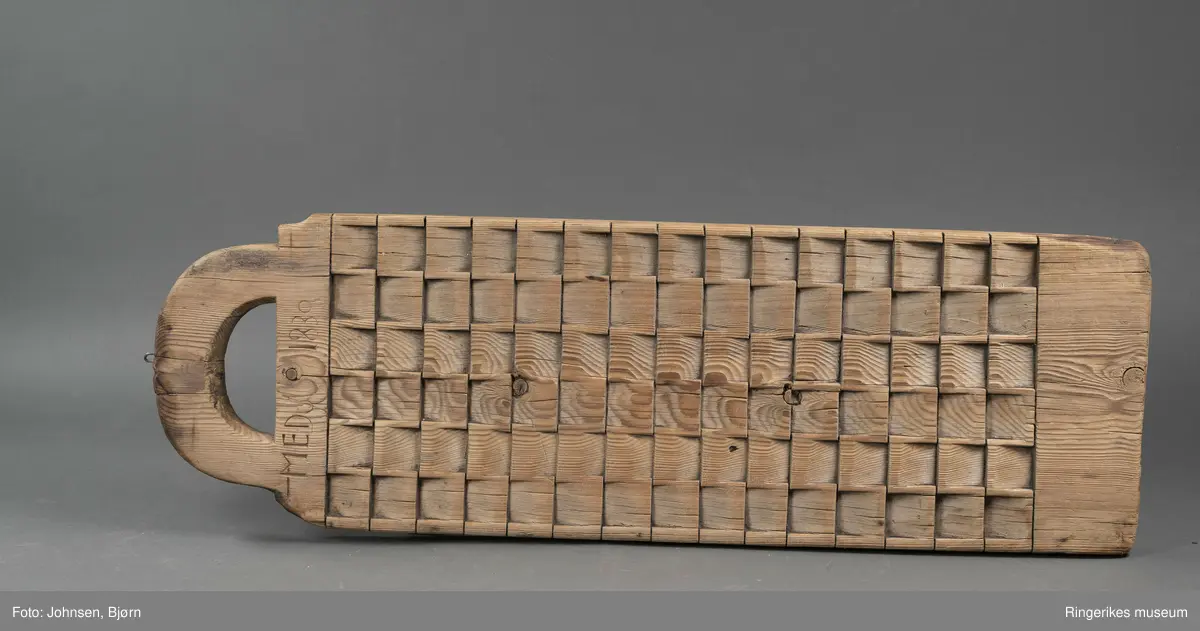 Vaskebrett i furu med kvadrater skråskjært i vekselsvis motsatt retning, sånn at rillene går i begge retninger. Håndtak øverst.