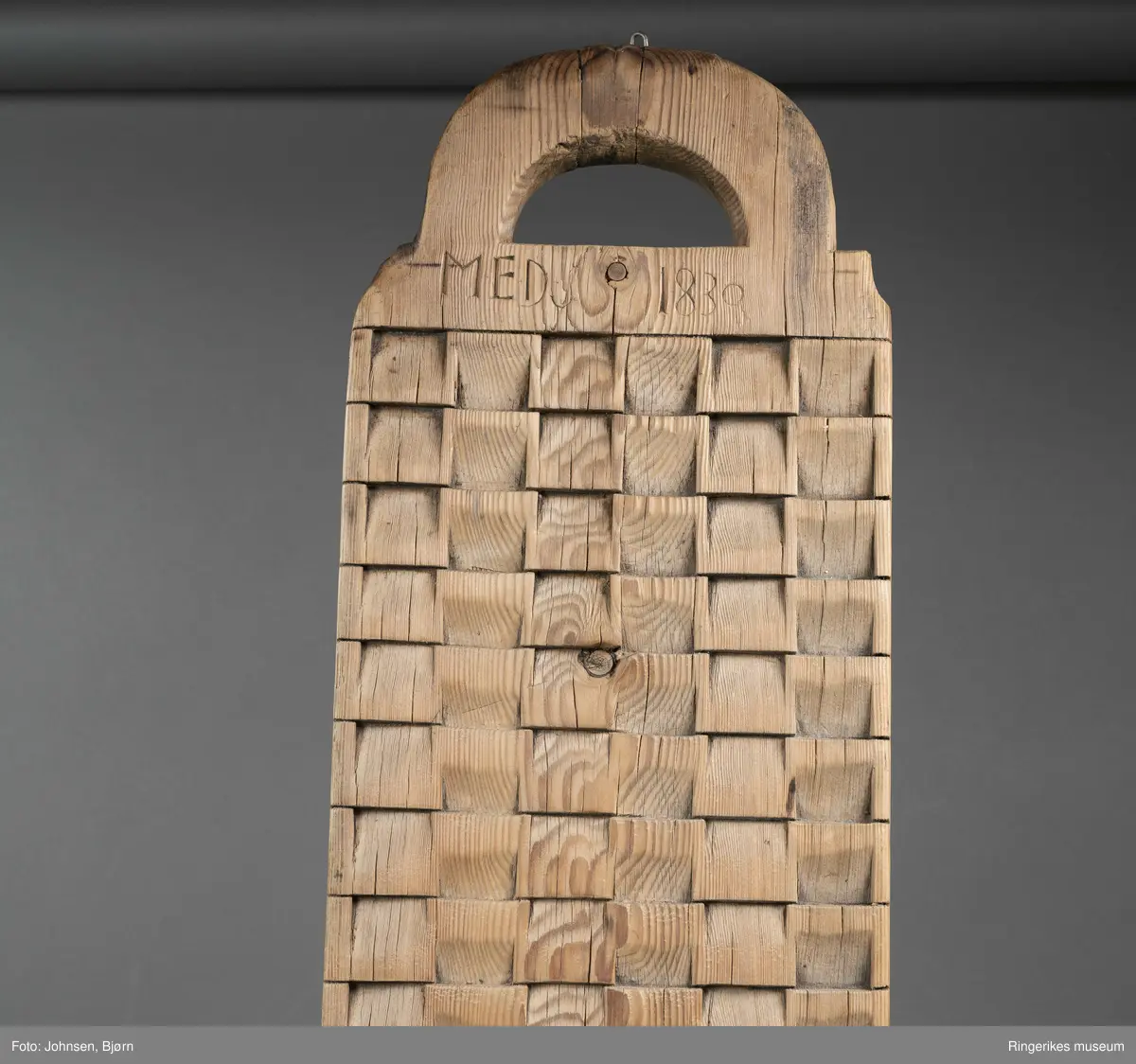 Vaskebrett i furu med kvadrater skråskjært i vekselsvis motsatt retning, sånn at rillene går i begge retninger. Håndtak øverst.