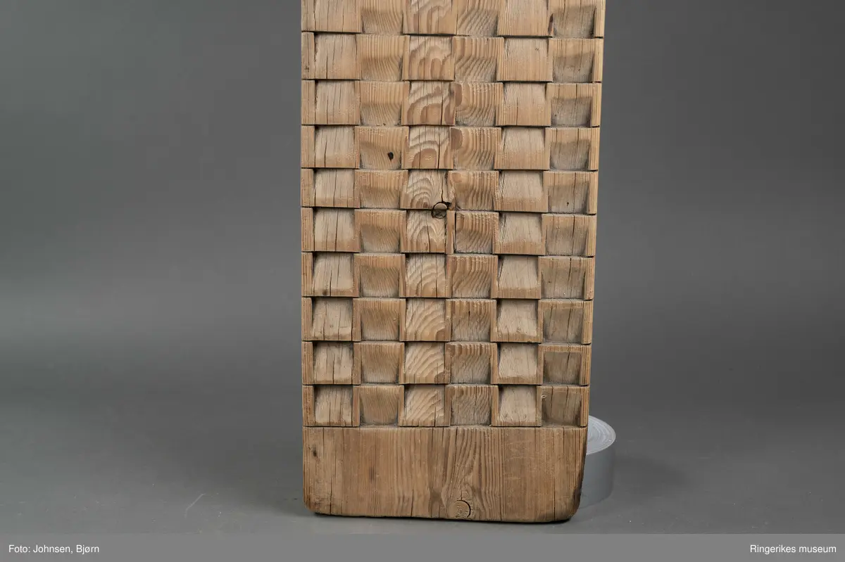 Vaskebrett i furu med kvadrater skråskjært i vekselsvis motsatt retning, sånn at rillene går i begge retninger. Håndtak øverst.