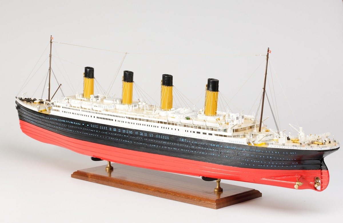 Oceanångare (Titanic) i trä och textil. Skrovet är målat i rött, svart och vitt, samt blått som är önsterventilerna. Däcket är trävitt och lackerat. På däcket finns detaljerat all utrustning såsom kranar, livbåtar, hytter, soffor och ventiler. Där finns fyra stora skorstenar med toppar i svart, och två större master med White Star Lines röda vimplar i toppen. Master och skorstenar är förbundna med linor i textil. I aktern är det tre propellrar och ett stort roder under vattenlinjen. Uppe vid relingen finns också en stång med en engelsk statsflagga. Modellen står på en brunbetsad platta i trä.