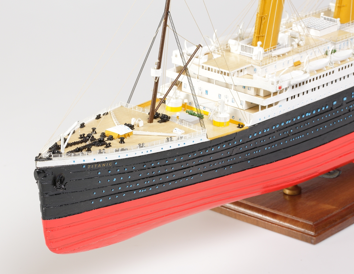 Oceanångare (Titanic) i trä och textil. Skrovet är målat i rött, svart och vitt, samt blått som är önsterventilerna. Däcket är trävitt och lackerat. På däcket finns detaljerat all utrustning såsom kranar, livbåtar, hytter, soffor och ventiler. Där finns fyra stora skorstenar med toppar i svart, och två större master med White Star Lines röda vimplar i toppen. Master och skorstenar är förbundna med linor i textil. I aktern är det tre propellrar och ett stort roder under vattenlinjen. Uppe vid relingen finns också en stång med en engelsk statsflagga. Modellen står på en brunbetsad platta i trä.