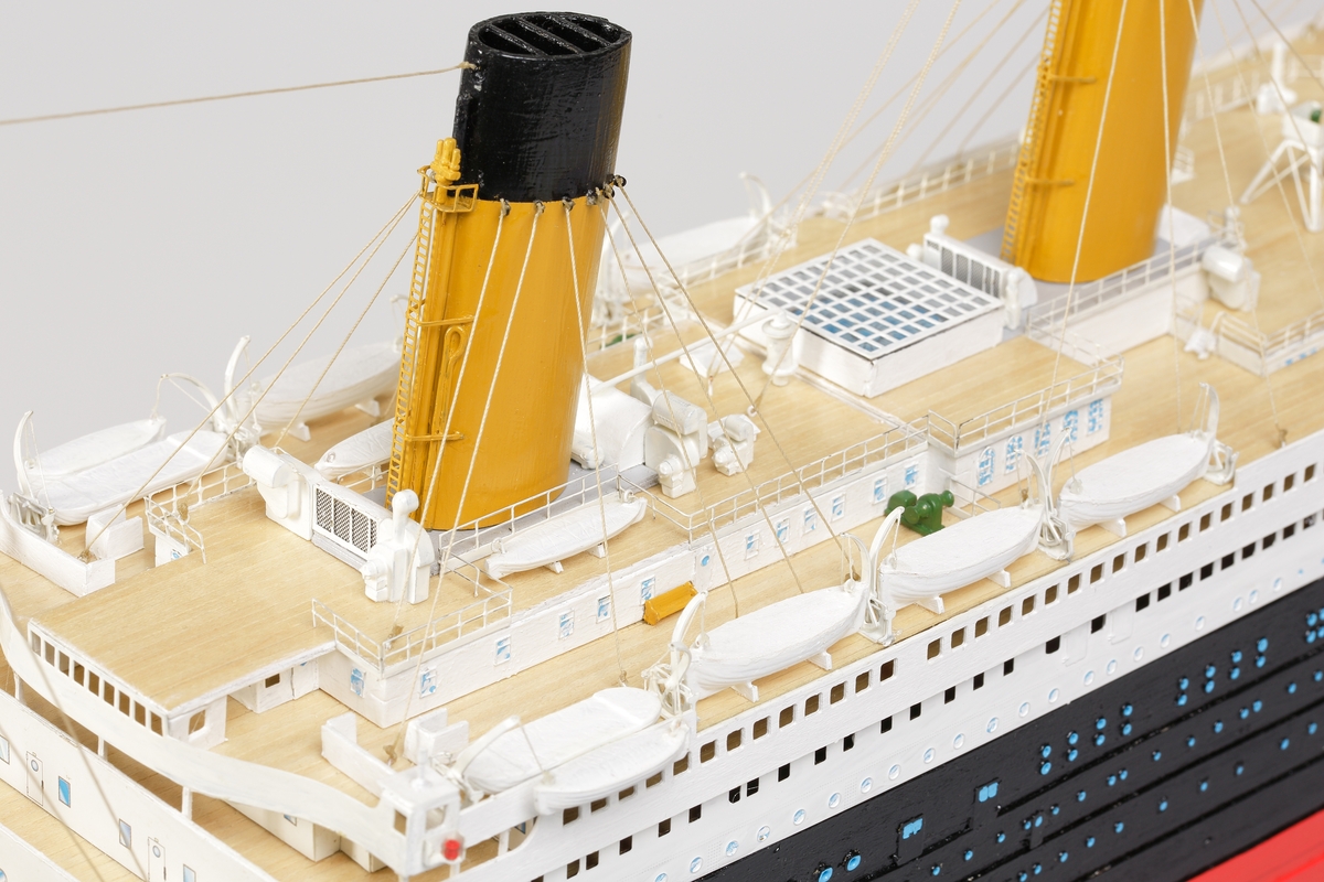 Oceanångare (Titanic) i trä och textil. Skrovet är målat i rött, svart och vitt, samt blått som är önsterventilerna. Däcket är trävitt och lackerat. På däcket finns detaljerat all utrustning såsom kranar, livbåtar, hytter, soffor och ventiler. Där finns fyra stora skorstenar med toppar i svart, och två större master med White Star Lines röda vimplar i toppen. Master och skorstenar är förbundna med linor i textil. I aktern är det tre propellrar och ett stort roder under vattenlinjen. Uppe vid relingen finns också en stång med en engelsk statsflagga. Modellen står på en brunbetsad platta i trä.