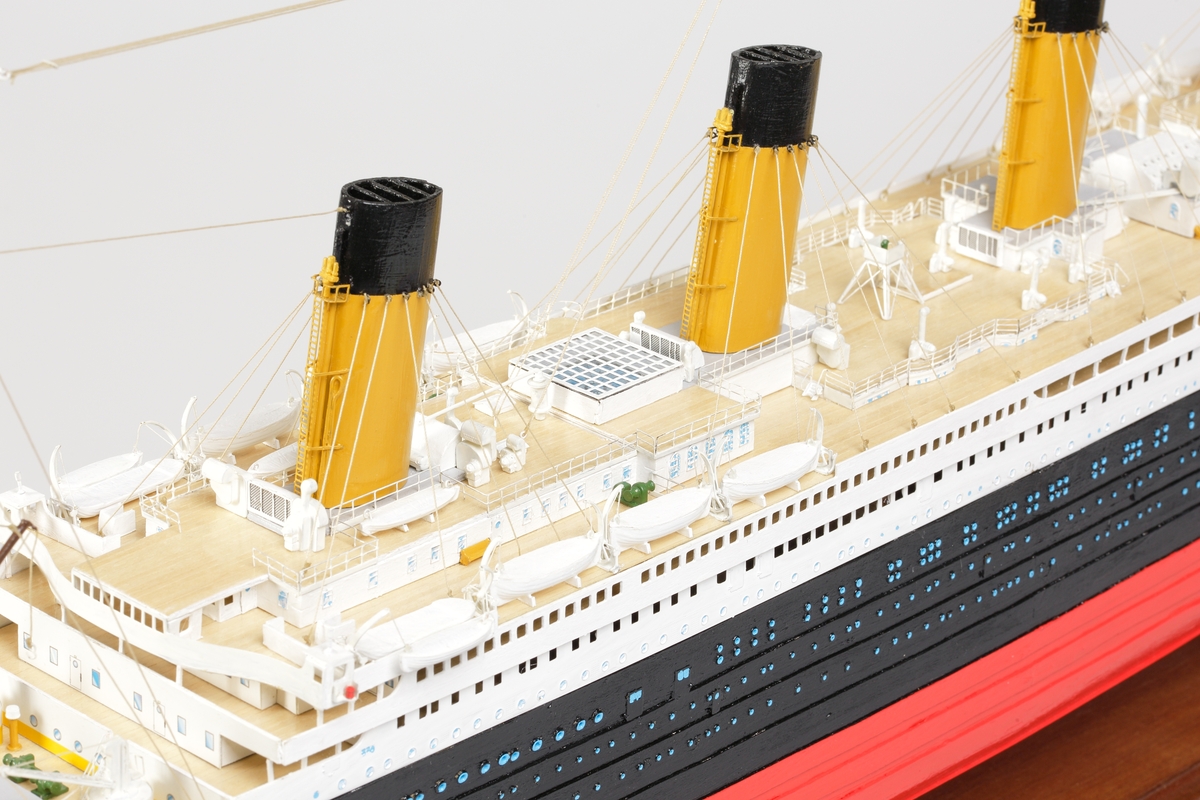 Oceanångare (Titanic) i trä och textil. Skrovet är målat i rött, svart och vitt, samt blått som är önsterventilerna. Däcket är trävitt och lackerat. På däcket finns detaljerat all utrustning såsom kranar, livbåtar, hytter, soffor och ventiler. Där finns fyra stora skorstenar med toppar i svart, och två större master med White Star Lines röda vimplar i toppen. Master och skorstenar är förbundna med linor i textil. I aktern är det tre propellrar och ett stort roder under vattenlinjen. Uppe vid relingen finns också en stång med en engelsk statsflagga. Modellen står på en brunbetsad platta i trä.