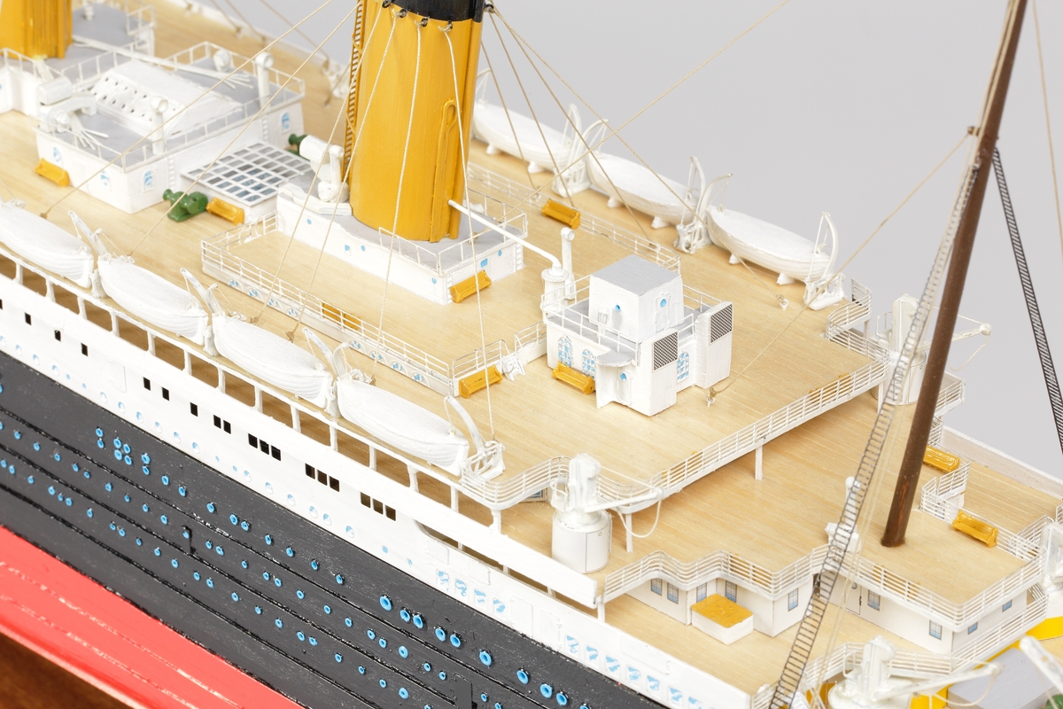 Oceanångare (Titanic) i trä och textil. Skrovet är målat i rött, svart och vitt, samt blått som är önsterventilerna. Däcket är trävitt och lackerat. På däcket finns detaljerat all utrustning såsom kranar, livbåtar, hytter, soffor och ventiler. Där finns fyra stora skorstenar med toppar i svart, och två större master med White Star Lines röda vimplar i toppen. Master och skorstenar är förbundna med linor i textil. I aktern är det tre propellrar och ett stort roder under vattenlinjen. Uppe vid relingen finns också en stång med en engelsk statsflagga. Modellen står på en brunbetsad platta i trä.
