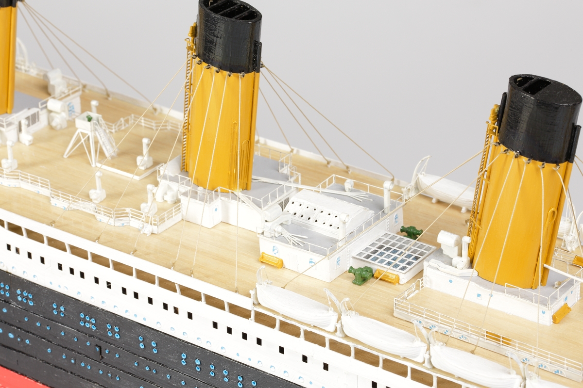 Oceanångare (Titanic) i trä och textil. Skrovet är målat i rött, svart och vitt, samt blått som är önsterventilerna. Däcket är trävitt och lackerat. På däcket finns detaljerat all utrustning såsom kranar, livbåtar, hytter, soffor och ventiler. Där finns fyra stora skorstenar med toppar i svart, och två större master med White Star Lines röda vimplar i toppen. Master och skorstenar är förbundna med linor i textil. I aktern är det tre propellrar och ett stort roder under vattenlinjen. Uppe vid relingen finns också en stång med en engelsk statsflagga. Modellen står på en brunbetsad platta i trä.