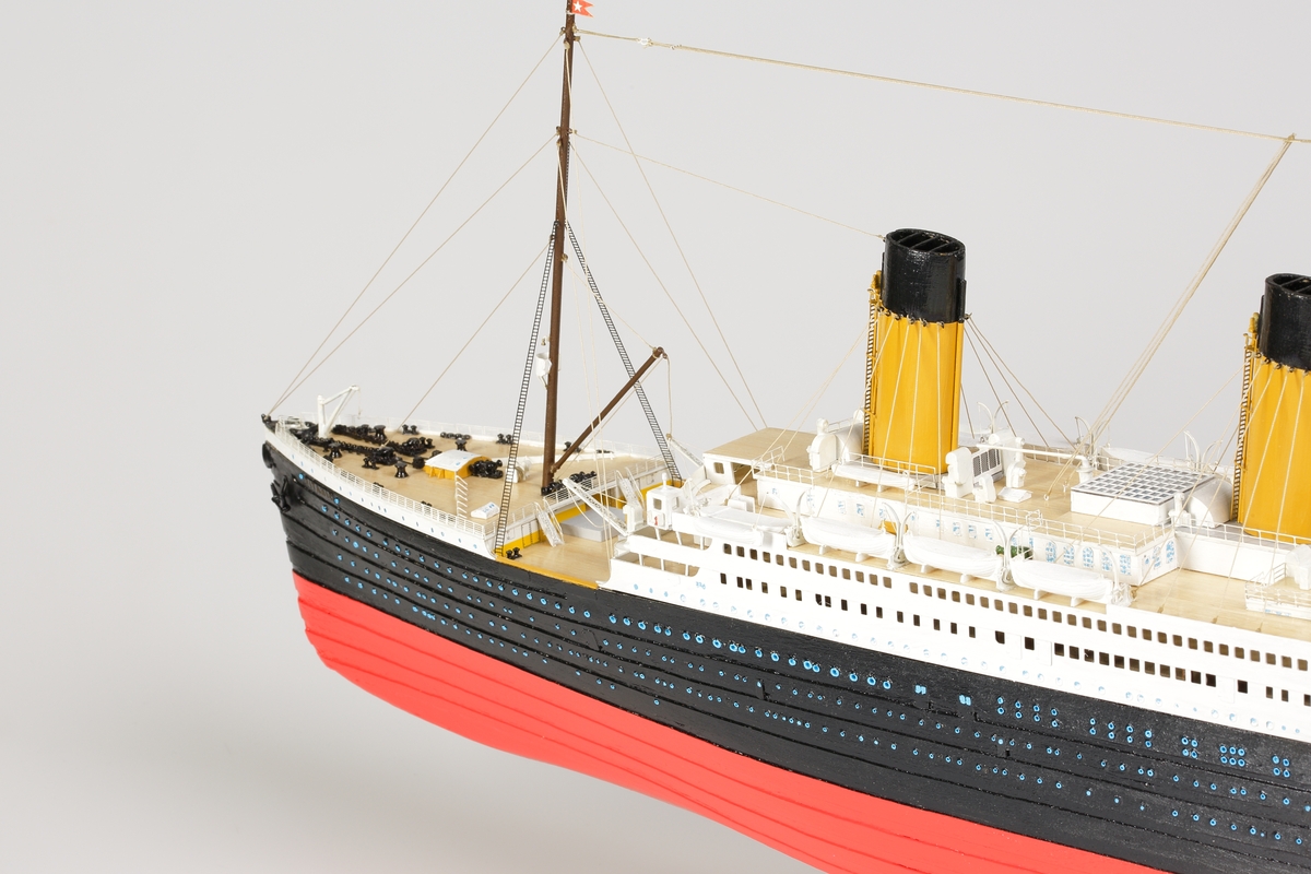 Oceanångare (Titanic) i trä och textil. Skrovet är målat i rött, svart och vitt, samt blått som är önsterventilerna. Däcket är trävitt och lackerat. På däcket finns detaljerat all utrustning såsom kranar, livbåtar, hytter, soffor och ventiler. Där finns fyra stora skorstenar med toppar i svart, och två större master med White Star Lines röda vimplar i toppen. Master och skorstenar är förbundna med linor i textil. I aktern är det tre propellrar och ett stort roder under vattenlinjen. Uppe vid relingen finns också en stång med en engelsk statsflagga. Modellen står på en brunbetsad platta i trä.