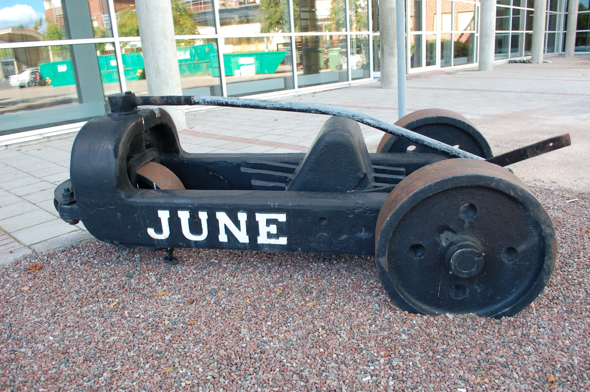 Svartmålad rivare, med text June vitmålad.  Massiv gjutjärnsram, massiva järnhjul, 2 bak, 1 fram. 3 rivtänder i mitten. dragring framtill.