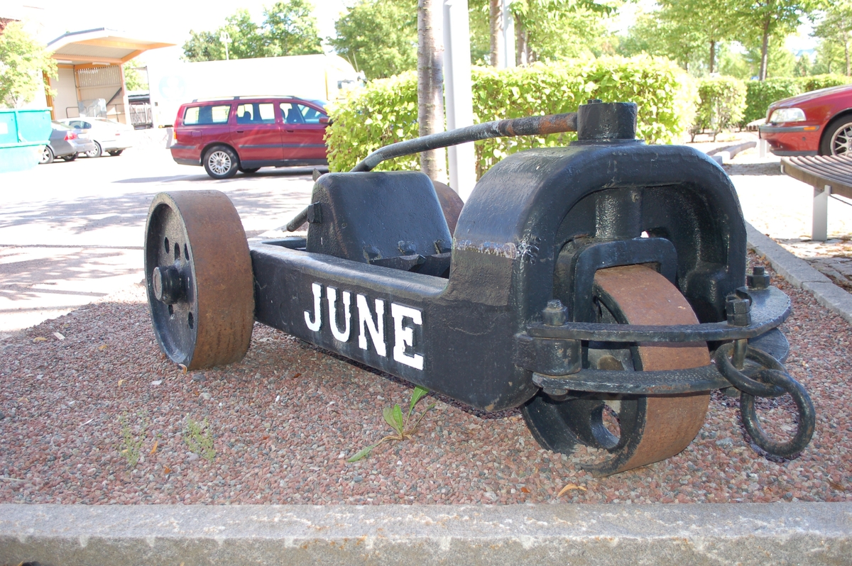 Svartmålad rivare, med text June vitmålad.  Massiv gjutjärnsram, massiva järnhjul, 2 bak, 1 fram. 3 rivtänder i mitten. dragring framtill.