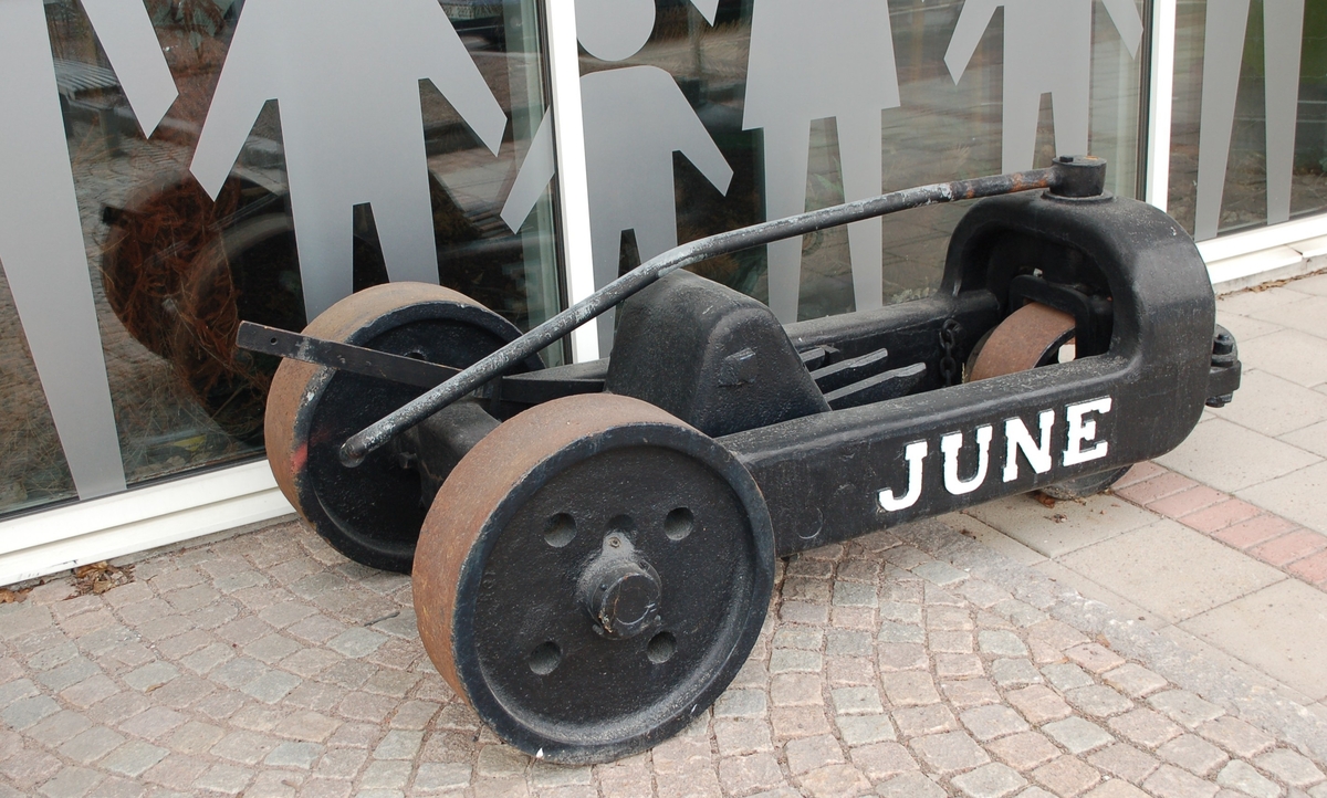 Svartmålad rivare, med text June vitmålad.  Massiv gjutjärnsram, massiva järnhjul, 2 bak, 1 fram. 3 rivtänder i mitten. dragring framtill.