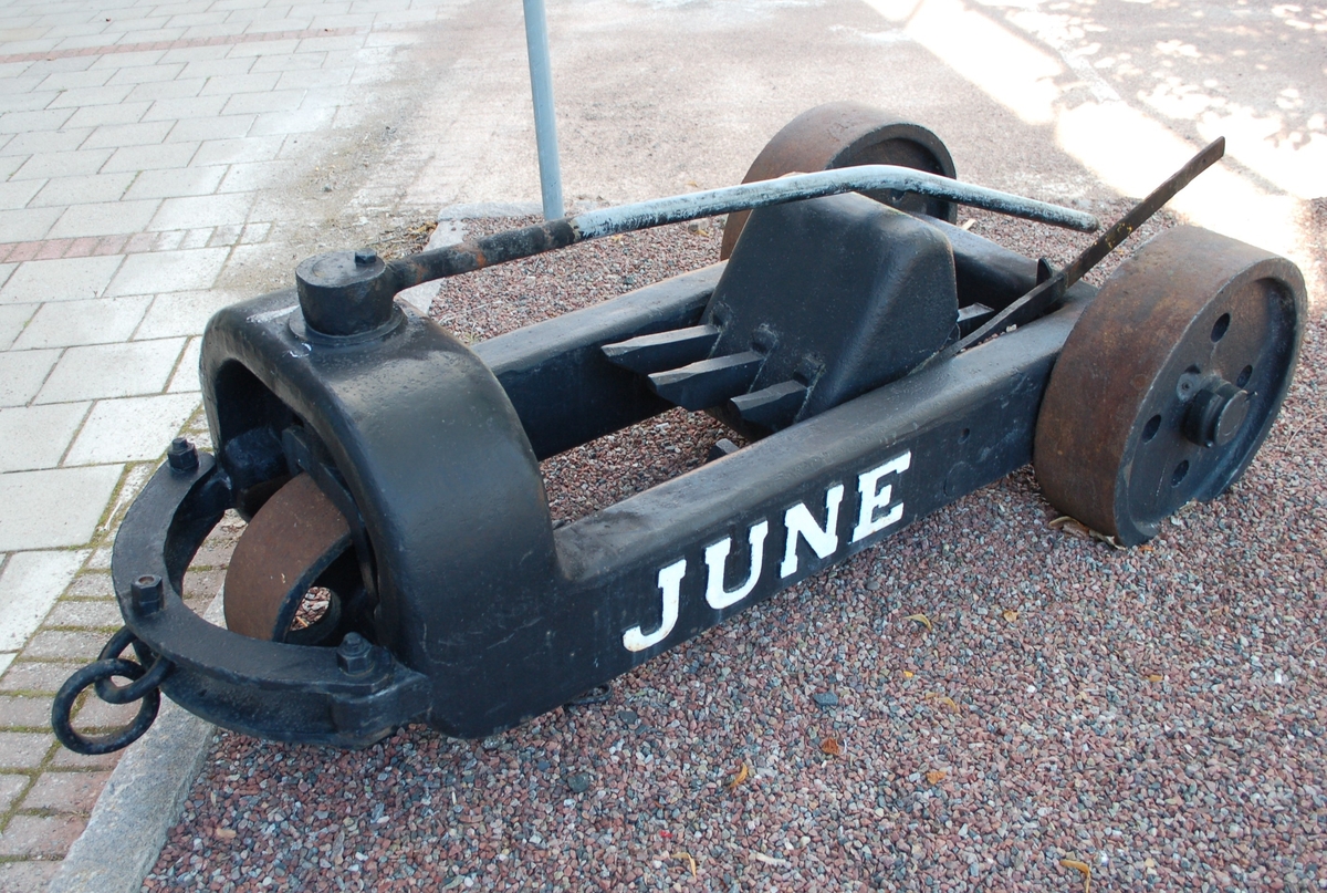 Svartmålad rivare, med text June vitmålad.  Massiv gjutjärnsram, massiva järnhjul, 2 bak, 1 fram. 3 rivtänder i mitten. dragring framtill.