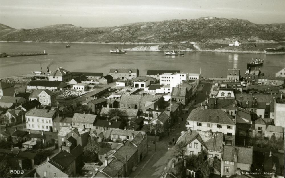 Postkort med motiv fra Bodø sentrum med havnen. Lille Hjartøya i bakgrunnen.