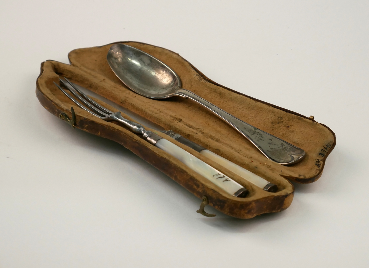 Ett etui med en uppsättning resebestick, kniv, gaffel och sked av silver. Kniv och gaffel med skaft av pärlemor.
Skeden dekorerad med monogram "FML" och stämplad med årsbokstav: F2=1788 samt "Eneroth" = guld- och silversmed Petter Eneroth (1741-1809) mästare från 1771.