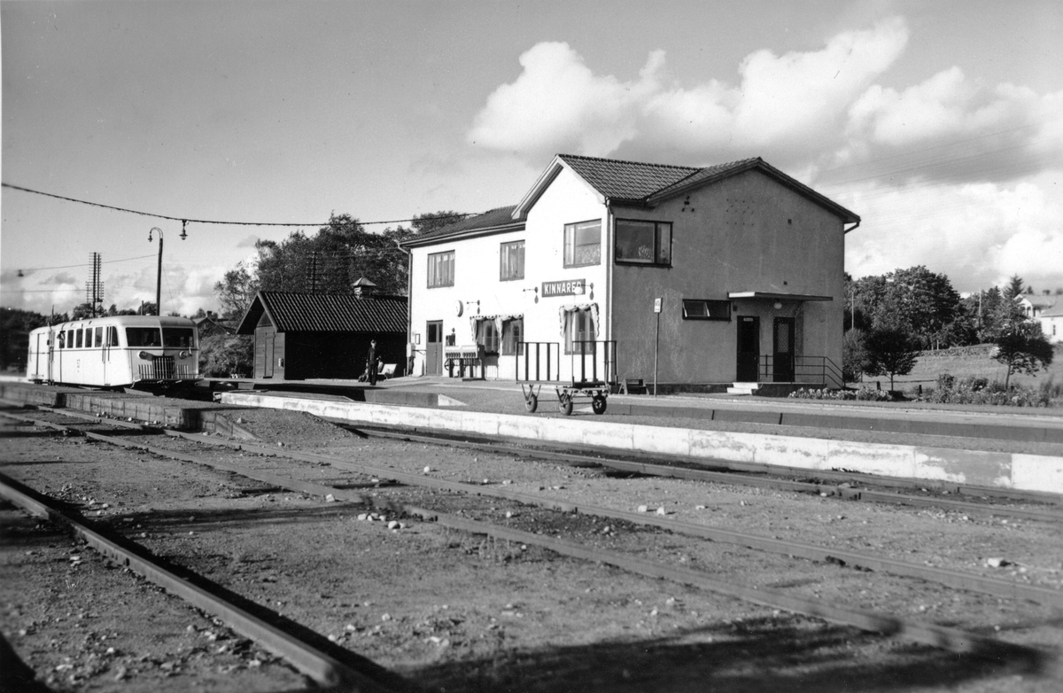 Vykort, "Kinnareds Järnvägsstation" i Hylte kommun. Stationen byggdes 1877 då sträckan Halmstad-Värnamo öppnades, men byggnaden har omgestaltats flera gånger tills den fick denna funktionalistiska dräkt. Stationen revs år 2000. Från Kinnared byggdes en järnväg till Fegen som invigdes 1885. Via Fegen-Ätrans Järnväg invigd 1887, och sedan Varberg-Ätrans Järnväg invigd 1911, kunde man komma vidare både till Varberg och Falkenberg härifrån.