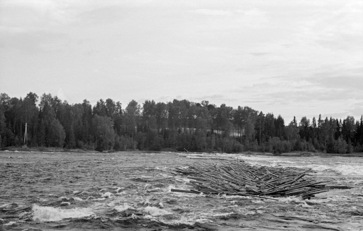 Tømmervase i den øvre delen av Funnefossen i Glomma, i den nordre delen av Nes kommune i Akershus. Fotografiet ble tatt i 1954. Funnefossen består egentlig av en serie trinn i Glommas elvefar, like etter at den har nådd Nes kommune på Romerike. Samlet fall er på bortimot 11 meter, fordelt på en drøyt 800 meter lang strekning. Fossen deles i to løp av en holme. Fløterne erfarte at det var enklest å få tømmeret gjennom det vestre løpet. Derfor ble det lagt ei lense på oversida av fossen som ledet stokkene i den retningen. Det hadde uansett lett for å sette seg en del tømmer i denne fossen, særlig når vannføringa i Glomma var lav, som da dette fotografiet ble tatt. I midten av 1870-åra ble det bygd et tresliperi ved Funnefossen.