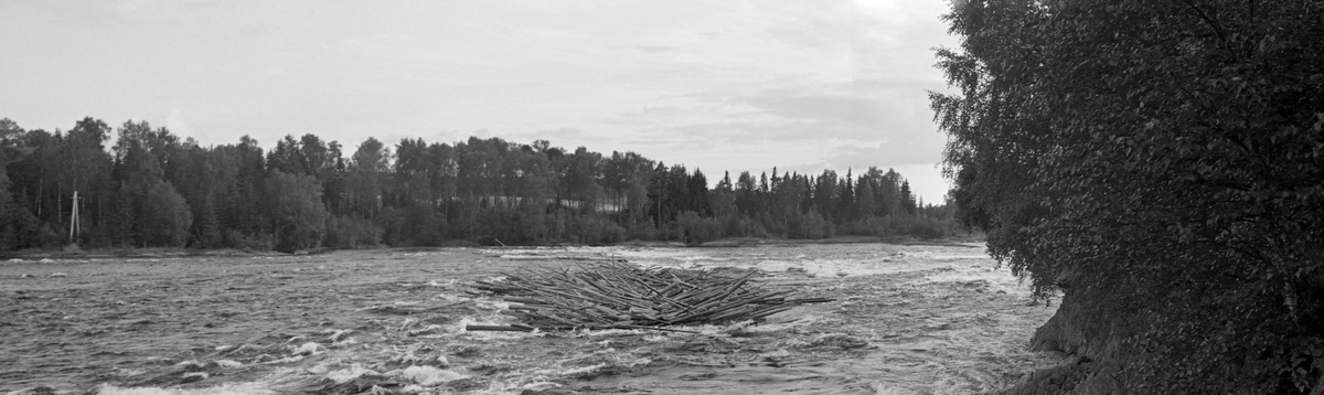 Tømmervase i den øvre delen av Funnefossen i Glomma, i den nordre delen av Nes kommune i Akershus. Fotografiet ble tatt i 1954. Funnefossen består egentlig av en serie trinn i Glommas elvefar, like etter at den har nådd Nes kommune på Romerike. Samlet fall er på bortimot 11 meter, fordelt på en drøyt 800 meter lang strekning. Fossen deles i to løp av en holme. Fløterne erfarte at det var enklest å få tømmeret gjennom det vestre løpet. Derfor ble det lagt ei lense på oversida av fossen som ledet stokkene i den retningen. Det hadde uansett lett for å sette seg en del tømmer i denne fossen, særlig når vannføringa i Glomma var lav, som da dette fotografiet ble tatt. I midten av 1870-åra ble det bygd et tresliperi ved Funnefossen.