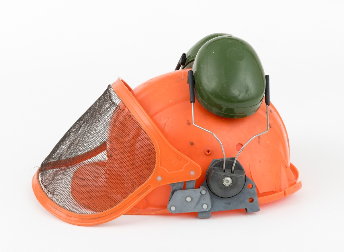 Hjelm, vernehjelm, hoggerhjelm, skogshjelm, for bruk under skogsarbeid. Hjelmen er støpt i hardplast. Den er utsyrt med visir og hørselvern (øreklokker). Det er flere sprekkdannelser hjelmens plastskall. Visirets netting har røket på to steder ved innfestingen i plastramma. Regulerbare reimer for tilpasning til brukerens hode mangler. 
Visir og hørselvern (øreklokker) er festet i samme "plastbrakett". Hørselvernene (øreklokkene) er regulerbare og kan svinges opp på hjelmen med en enkel håndbevegelse. (Hørselvern og visir kan for registrator se ut til å være av noe nyere dato enn selve hjelmen, men det er ikke bekreftet. ) Hørselvernene har for øvrig skomgummpolstring som ligger an mot brukerens ører. 
Hjelmen har to luftehull på hver side som kan åpnes og lukkes med vridbare plastklaffer. Klaffene betjenes fra innsiden.