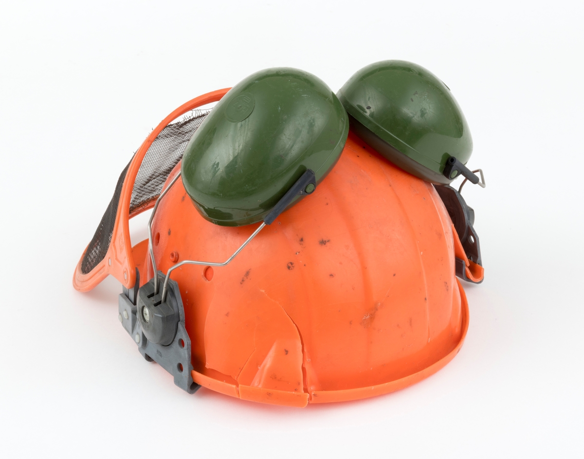 Hjelm, vernehjelm, hoggerhjelm, skogshjelm, for bruk under skogsarbeid. Hjelmen er støpt i hardplast. Den er utsyrt med visir og hørselvern (øreklokker). Det er flere sprekkdannelser hjelmens plastskall. Visirets netting har røket på to steder ved innfestingen i plastramma. Regulerbare reimer for tilpasning til brukerens hode mangler. 
Visir og hørselvern (øreklokker) er festet i samme "plastbrakett". Hørselvernene (øreklokkene) er regulerbare og kan svinges opp på hjelmen med en enkel håndbevegelse. (Hørselvern og visir kan for registrator se ut til å være av noe nyere dato enn selve hjelmen, men det er ikke bekreftet. ) Hørselvernene har for øvrig skomgummpolstring som ligger an mot brukerens ører. 
Hjelmen har to luftehull på hver side som kan åpnes og lukkes med vridbare plastklaffer. Klaffene betjenes fra innsiden.