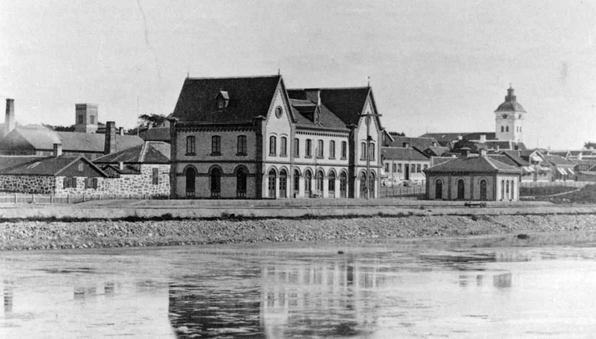 En tidig bild av järnvägsstationen i Varberg som uppfördes av Varberg-Borås järnväg, invigd den 1 november 1880; stadens första järnvägsförbindelse. Alla stationshus på sträckan ritades av ingenjör J A Tistrand, men endast Varbers station uppfördes av sten och på entreprenad av byggmästare L Forsberg från Göteborg. Bangården anlades på en utfyllnad av havsviken så ursprungligen gick vattnet så här nära inpå. Även den lilla byggnaden till höger finns ännu kvar.
T v syns Varbergs Mekaniska Verkstad, etablerad i mitten av 1800-talet. Tornet som reser sig bakom är lusthuset Malakoff uppfört av konsul P S Bagge i hans trädgård. Huset t h mellan järnvägsstationen och kyrkan är järnvägshotellet. Fastigheten med det valmade, höga taket är Torellska huset, nuvarande Gästis.