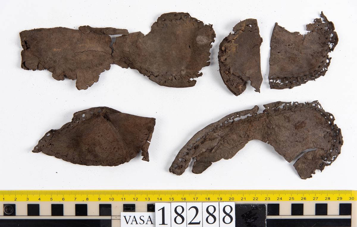Åtta större delar samt ett hundratal fragment från sko: del av skobotten, bakkappa, fragmentariska sulor, ovanläder, inlägg, sidostycke mm.

En bit av ovanlädret sitter fästat med skopligg vid skobottnen.

Ett fragmentariskt sidostycke. Nedanför styckets övre ytterkant syns två inristade linjer.

Lädret är mycket fragmentariskt och sprött och flera av delarna och fragmenten ligger hopvikta.