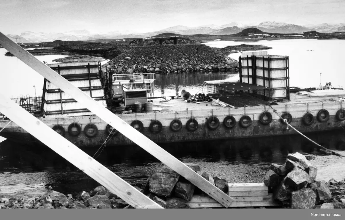 brubygging med lekter, antakelig Dampleia på Smøla. Dampleibrua er en spennbetongbro på fylkesvei 669 mellom øyene Lamøya og Rossvolløya i Smøla kommune i Møre og Romsdal. Brua krysser sundet Dampleia, er 161 meter lang, og lengste spenn er 35 meter. Bildet er fra avisa Tidens Krav sitt arkiv i tidsrommet 1970-1994. Nå i Nordmøre museums fotosamling.