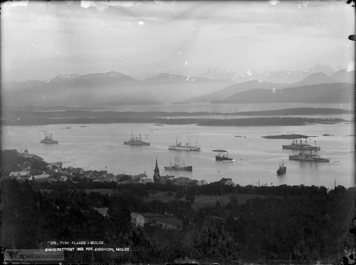 Molde by sett fra nord., "225. Tysk flaade i Molde" Molde med skip på fjorden. 225. .Tysk flåte på besøk i Molde..SMY Hohenzollern er det hvite skipet i midten...Det største flåtebesøk var i 1904. Keiser Wilhelm II hadde vært i Molde noen dager bare ledsaget av krysseren Hamburg og jageren Sleipner. Så kom 5 store dampskip med kull, og endelig en flåte av Tysklands største og mest moderne krigsskip, foruten depesjeskip og torpedobåter. Flåten hadde 6000 manns besetning..Det lå over 30 store fartøyer på Molde havn i ca 14 dager. .SMY Hohenzollern er det hvite skipet i midten.