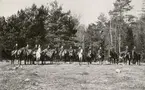 En grupp ryttare har ställt upp sig för fotografering på en äng. Runt 1900.