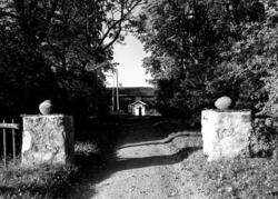 Kraftiga grindstolpar i sten med Kila prästgård i bakgrunden