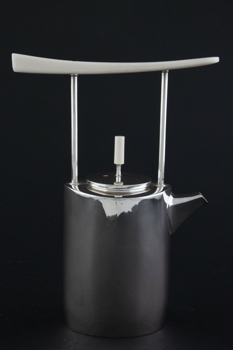 Kaffekanne i sølv. Ovalformet korpus med lett bølgende vegger og liten tut. Fra skulderen reiser det seg to tynne rør som forbinder kannen med et håndtak i elfenben. Sirkulært lokk med sylinderformet lokknapp i elfenben. 