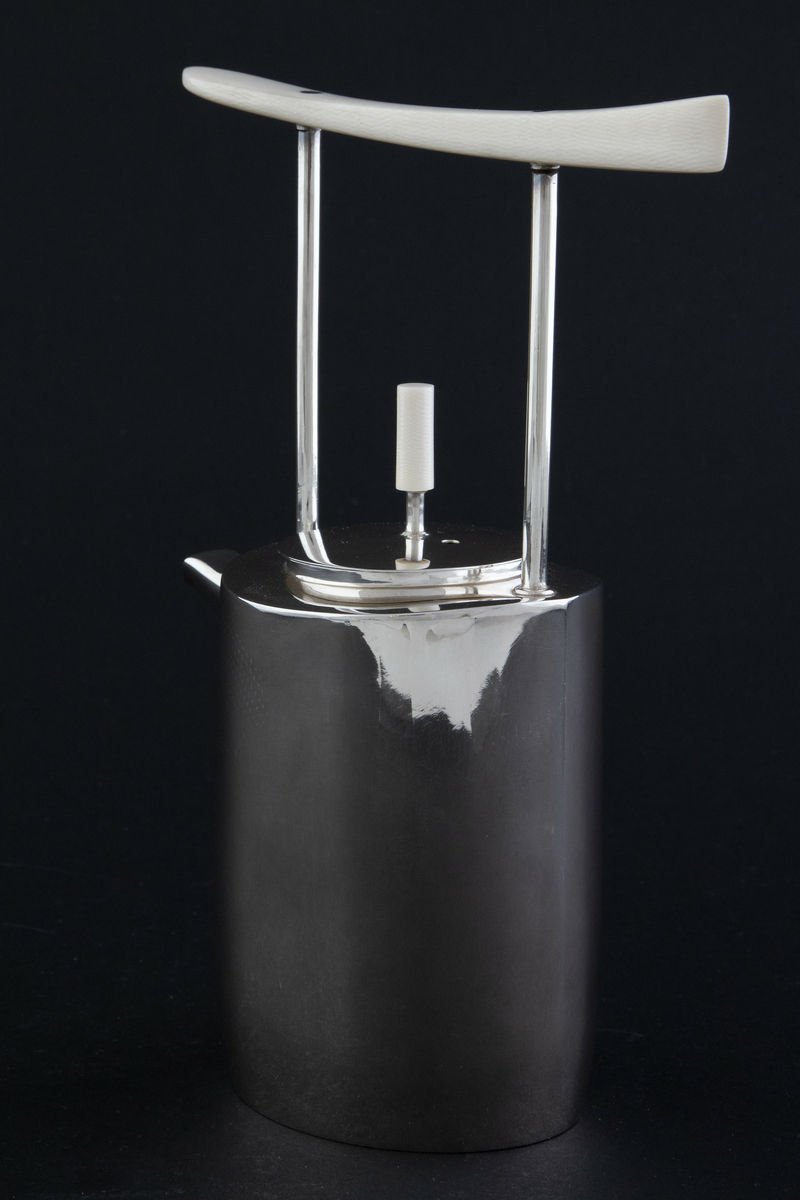 Kaffekanne i sølv. Ovalformet korpus med lett bølgende vegger og liten tut. Fra skulderen reiser det seg to tynne rør som forbinder kannen med et håndtak i elfenben. Sirkulært lokk med sylinderformet lokknapp i elfenben. 