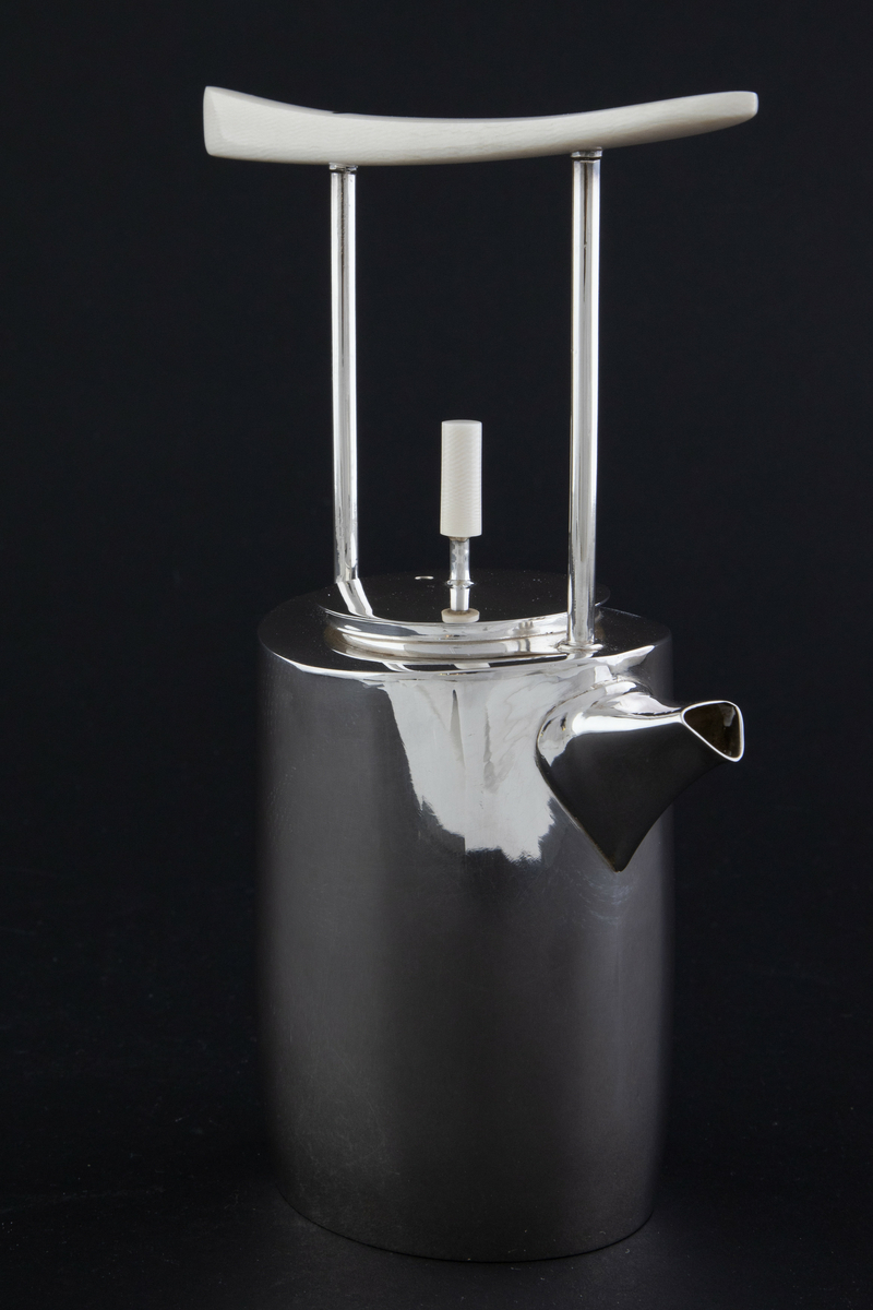 Kaffekanne i sølv. Ovalformet korpus med lett bølgende vegger og liten tut. Fra skulderen reiser det seg to tynne rør som forbinder kannen med et håndtak i elfenben. Sirkulært lokk med sylinderformet lokknapp i elfenben. 