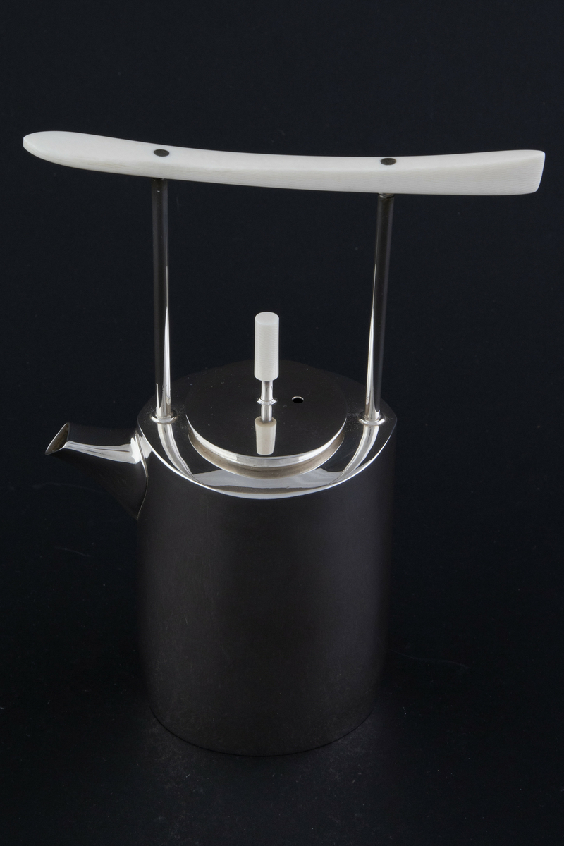 Kaffekanne i sølv. Ovalformet korpus med lett bølgende vegger og liten tut. Fra skulderen reiser det seg to tynne rør som forbinder kannen med et håndtak i elfenben. Sirkulært lokk med sylinderformet lokknapp i elfenben. 