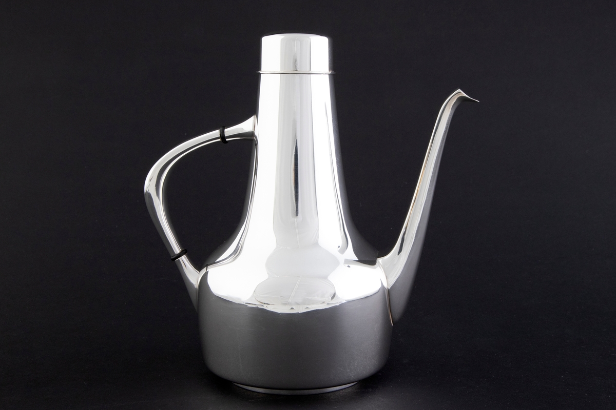 Kaffekanne som er utført i glattpolert sølv, uten dekor og med myke kanter. Sylinderformet kompakt korpus, som glir over i en konisk langstrakt hals. Fra korpus løper en lang tynn tut, som er mykt buet. Det sirkulære lokket fremstår som en forlengelse av halsen, men overgangen er anntydet med en ringformet vulst. Den buede haken løper fra korpus til øvre del av halsen, og før ansatsene er det plassert to ringformede lameller av presstoff for varmeisolering. 