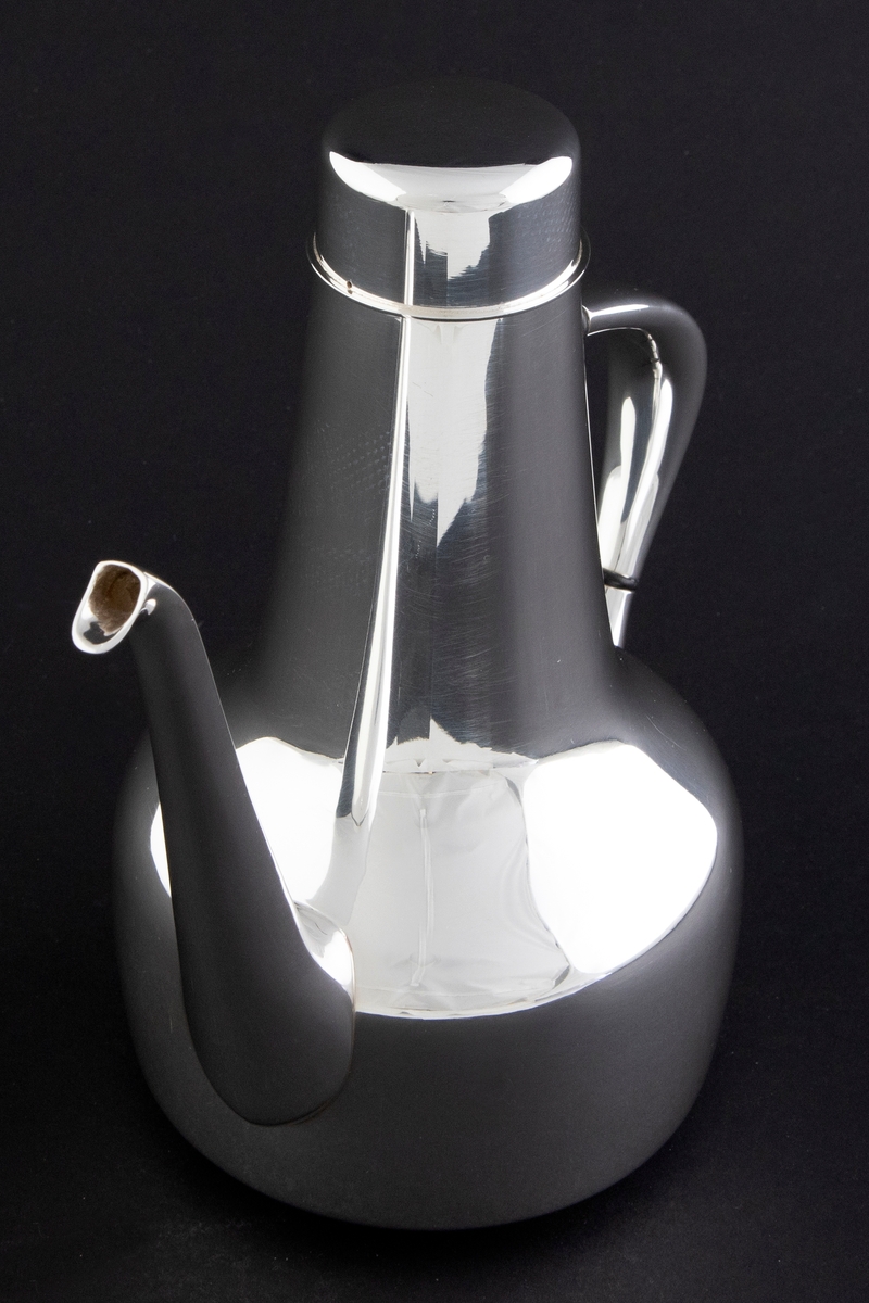 Kaffekanne som er utført i glattpolert sølv, uten dekor og med myke kanter. Sylinderformet kompakt korpus, som glir over i en konisk langstrakt hals. Fra korpus løper en lang tynn tut, som er mykt buet. Det sirkulære lokket fremstår som en forlengelse av halsen, men overgangen er anntydet med en ringformet vulst. Den buede haken løper fra korpus til øvre del av halsen, og før ansatsene er det plassert to ringformede lameller av presstoff for varmeisolering. 