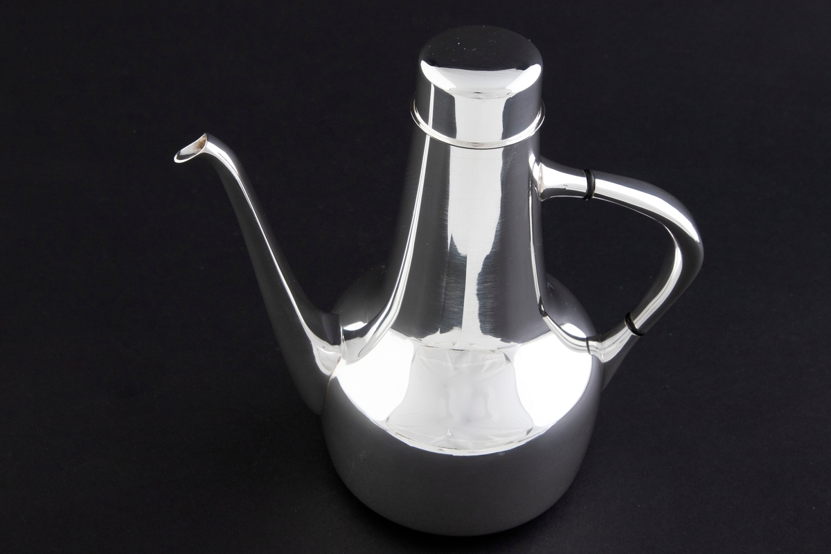 Kaffekanne som er utført i glattpolert sølv, uten dekor og med myke kanter. Sylinderformet kompakt korpus, som glir over i en konisk langstrakt hals. Fra korpus løper en lang tynn tut, som er mykt buet. Det sirkulære lokket fremstår som en forlengelse av halsen, men overgangen er anntydet med en ringformet vulst. Den buede haken løper fra korpus til øvre del av halsen, og før ansatsene er det plassert to ringformede lameller av presstoff for varmeisolering. 