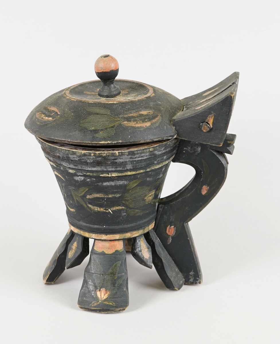 Dreia smørkanne, med påsett lok og hank. Fire føt. Heilt i tre. Korpus har rundt tverrsnitt, og utskrånande sider oppover. Loket er hengsla med ein trenagl øvst i hanken. Innvendig er loket dekorert med utskore mønster. Heile utsida er dekormåla. Føtene er skore ut i same emne som kanna, samt fire "tappar" mellom føtene - til dekor. Laus botnplate ligg inni.