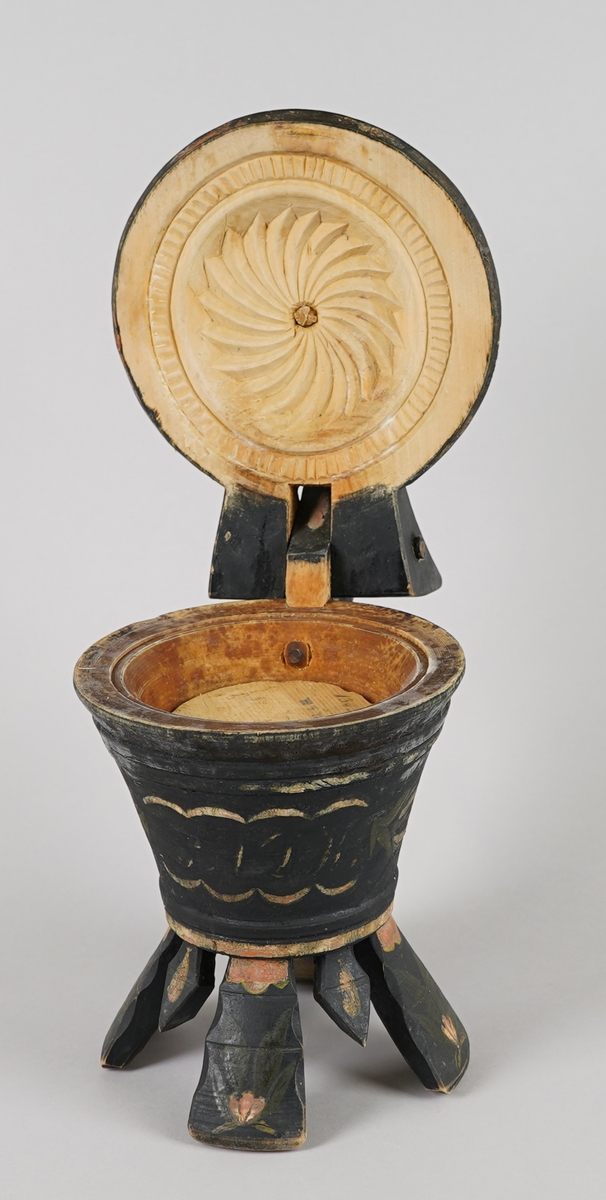 Dreia smørkanne, med påsett lok og hank. Fire føt. Heilt i tre. Korpus har rundt tverrsnitt, og utskrånande sider oppover. Loket er hengsla med ein trenagl øvst i hanken. Innvendig er loket dekorert med utskore mønster. Heile utsida er dekormåla. Føtene er skore ut i same emne som kanna, samt fire "tappar" mellom føtene - til dekor. Laus botnplate ligg inni.