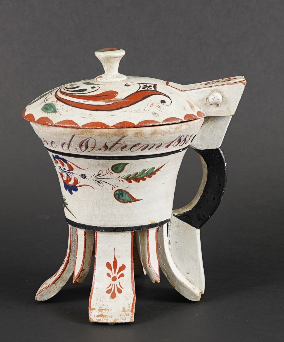 Dreia smørkanne, med påsett lok og hank. Fire føt. Heilt i tre. Korpus har rundt tverrsnitt, og utskrånande sider oppover. Loket er hengsla med ein trenagl øvst i hanken. Innvendig er loket dekorert med utskore mønster. Heile utsida er dekormåla. Føtene er skore ut i same emne som kanna, samt fire "tappar" mellom føtene - til dekor. Gjennomgåande hol i botn, for å hindre oppsprekking ved tørking.