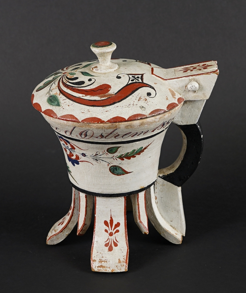 Dreia smørkanne, med påsett lok og hank. Fire føt. Heilt i tre. Korpus har rundt tverrsnitt, og utskrånande sider oppover. Loket er hengsla med ein trenagl øvst i hanken. Innvendig er loket dekorert med utskore mønster. Heile utsida er dekormåla. Føtene er skore ut i same emne som kanna, samt fire "tappar" mellom føtene - til dekor. Gjennomgåande hol i botn, for å hindre oppsprekking ved tørking.