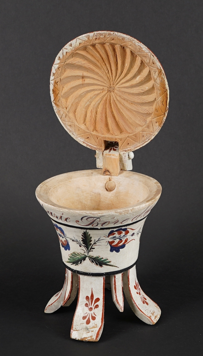 Dreia smørkanne, med påsett lok og hank. Fire føt. Heilt i tre. Korpus har rundt tverrsnitt, og utskrånande sider oppover. Loket er hengsla med ein trenagl øvst i hanken. Innvendig er loket dekorert med utskore mønster. Heile utsida er dekormåla. Føtene er skore ut i same emne som kanna, samt fire "tappar" mellom føtene - til dekor. Gjennomgåande hol i botn, for å hindre oppsprekking ved tørking.