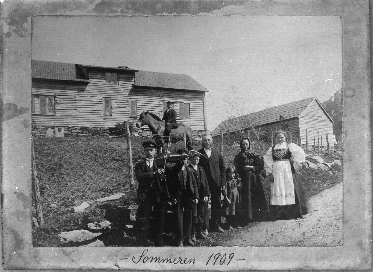 Gardstunet på garden Oppheim i Ølen, sommaren 1909. På hesteryggen sit Lars Opheim. Langs vegen frå venstre: Mikkel Opheim (med fela), Odd Opheim, Andreas Opheim, Mikkel Opheim (far), Randi Opheim, Ragnhild Opheim (mor) og Steinvor Opheim.