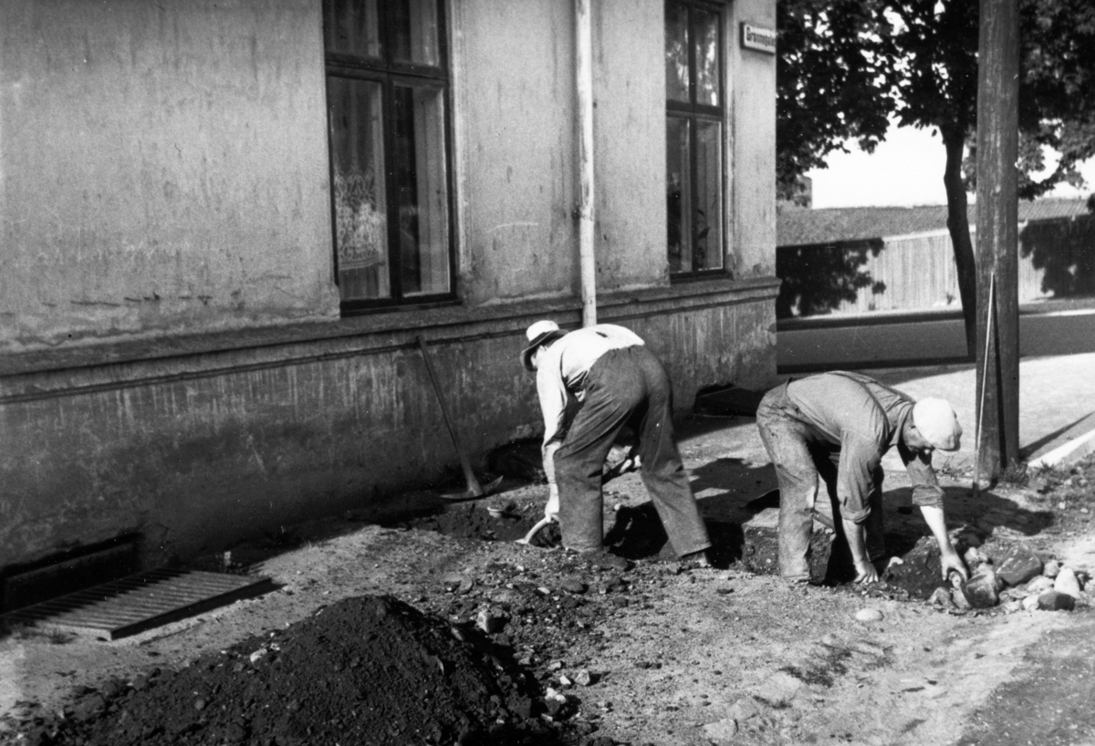 Arbeidere, ukjente, gaver grøft med spade,hakke, I Kirkebakken/Grønnegata, Hamar. Grøftearbeidere, kroppsarbeid, redskaper, arbeidsklær, 1940-årene.