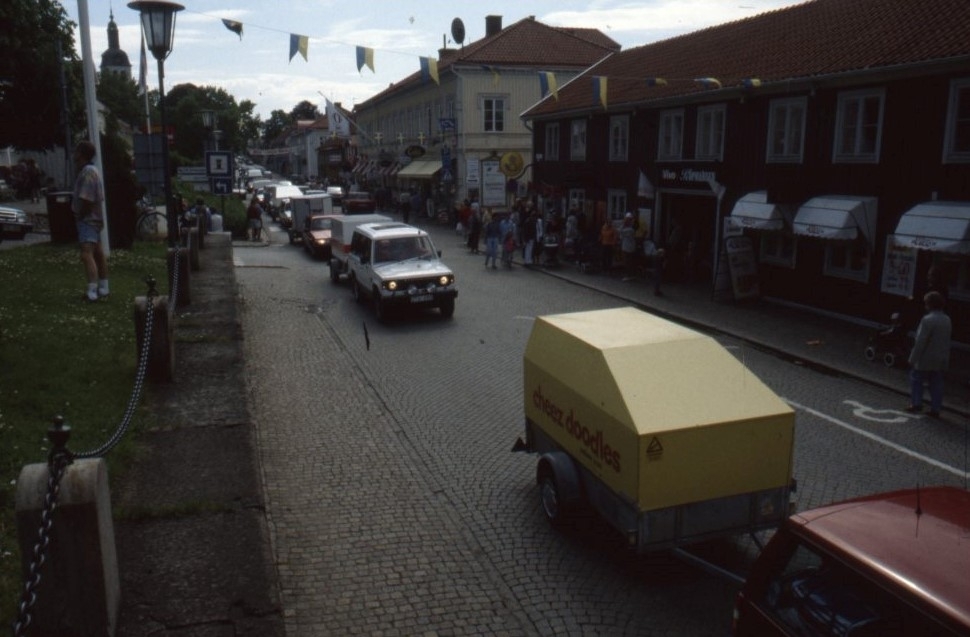 Vy över Brahegatan där en kortege av bilar med släp följer orkestern.