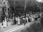 Folksamling på Brahegatan vid Söder tull. Flaggspel, hissade flaggor och en grönklädd båge över vägen med text: 