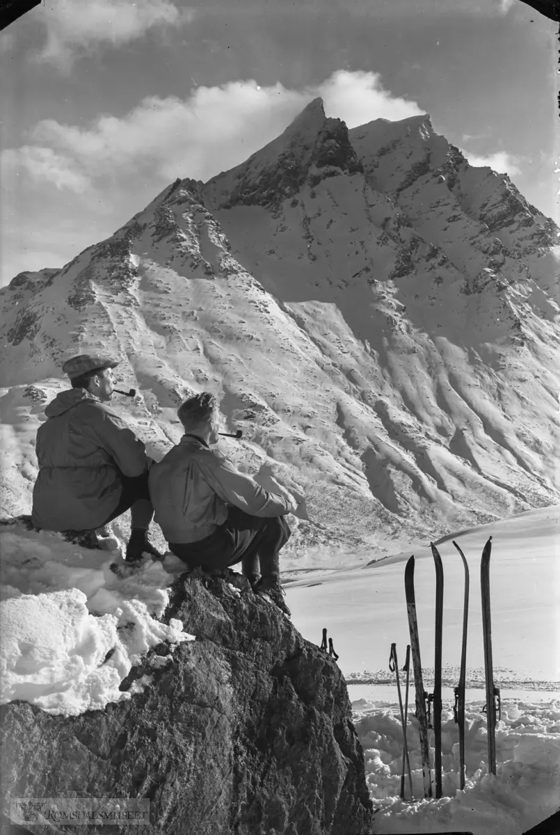 To skituristar har røykepause på ein stor stein. Store Vengetind i bakgrunnen.