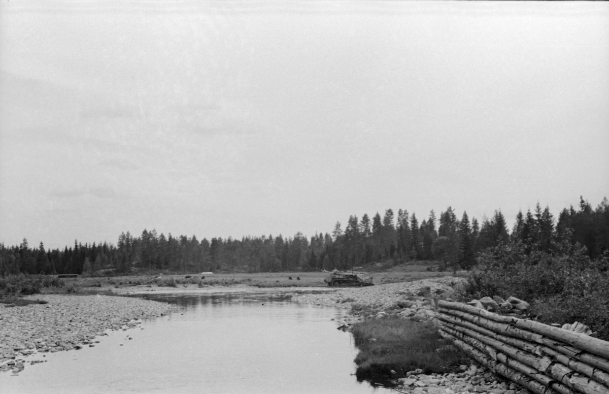 Bulldoserarbeid ved Bergesæterfløyta i Juråvassdraget i Nord-Odal i Hedmark sommeren 1955. Fotografiet er antakelig tatt fra Bergsæterdammen i motstrøms retning mot det som i sommersesongen skulle være et vannreservoar for tømmerfløtinga i det nevnte vassdraget. Etter 2. verdenskrig kunne Glomma fellesfløtingsforening leie bulldosere som skulle bidra til å tilpasse vassdragstopografien til virksomhetens behov. Her forsøkte man antakelig å øke volumet på det vannmagasinet Bergesæterdammen kunne magasinere ved å skyve masse vekk fra dambotnen. I fløtingssesongen skulle antakelig tømmerskådammen til høyre i forgrunnen lede stokkene mot damløpet. 

Juråa kommer fra Gåsvatna i Nord-Odal (om lag 450 meter over havet) og renner først sørover mot Skurvsjøen, derfra sørvestover. Den forenes først med Grytåa, og i grenda Mo i Nord-Odal renner den også saman med Tannåa. Under navnet Moelva flyter vannet fra disse tre åene etter hvert ut i Storsjøen (om lag 130 meter over havet). Den nevnte elvestrekningen hadde tidlig på 1900-tallet fem dammer: Øvre og Nedre Gåsvassdam, Skurvsjødammen, Bergesæterdammen og Dalssæterdammen. I 1950-åra, da dette fotografiet ble tatt, var Øvre Gåsvassdam ute av funksjon (jfr. SJF.1990-02406). I 1955 ble det innmeldt 103 505 tømmerstokker til fløting i Juråa.