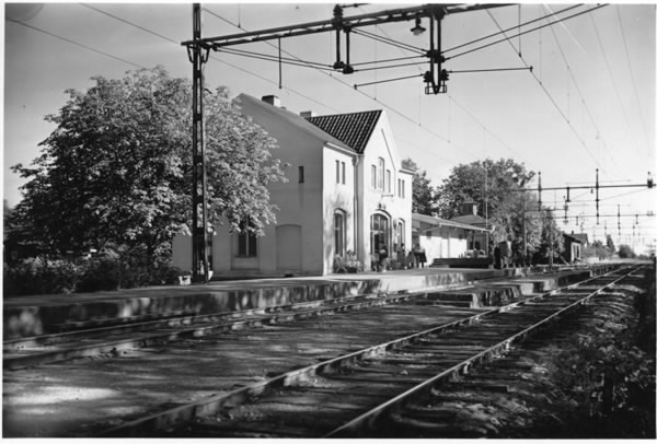 Spårområde vid Långås järnvägsstation. Väntande människor på perrongen, både sittande och stående.