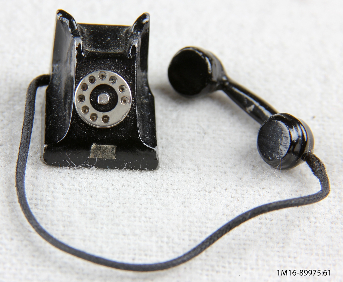 Telefon av metall, svartmålad, sifferskivan omålad. För dockskåp.