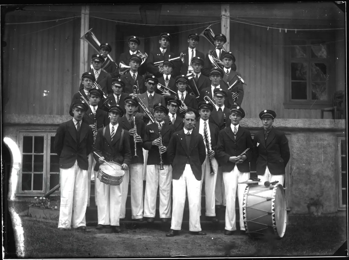 Jevnaker musikkforening med instrumenter står oppstilt foran et inngangsparti.